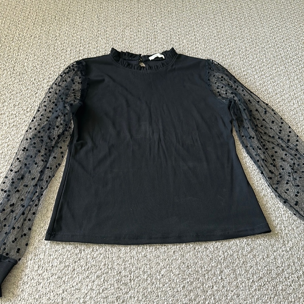 Black, high neck, puff-sleeved top. Sleeves are sheer with polka dots